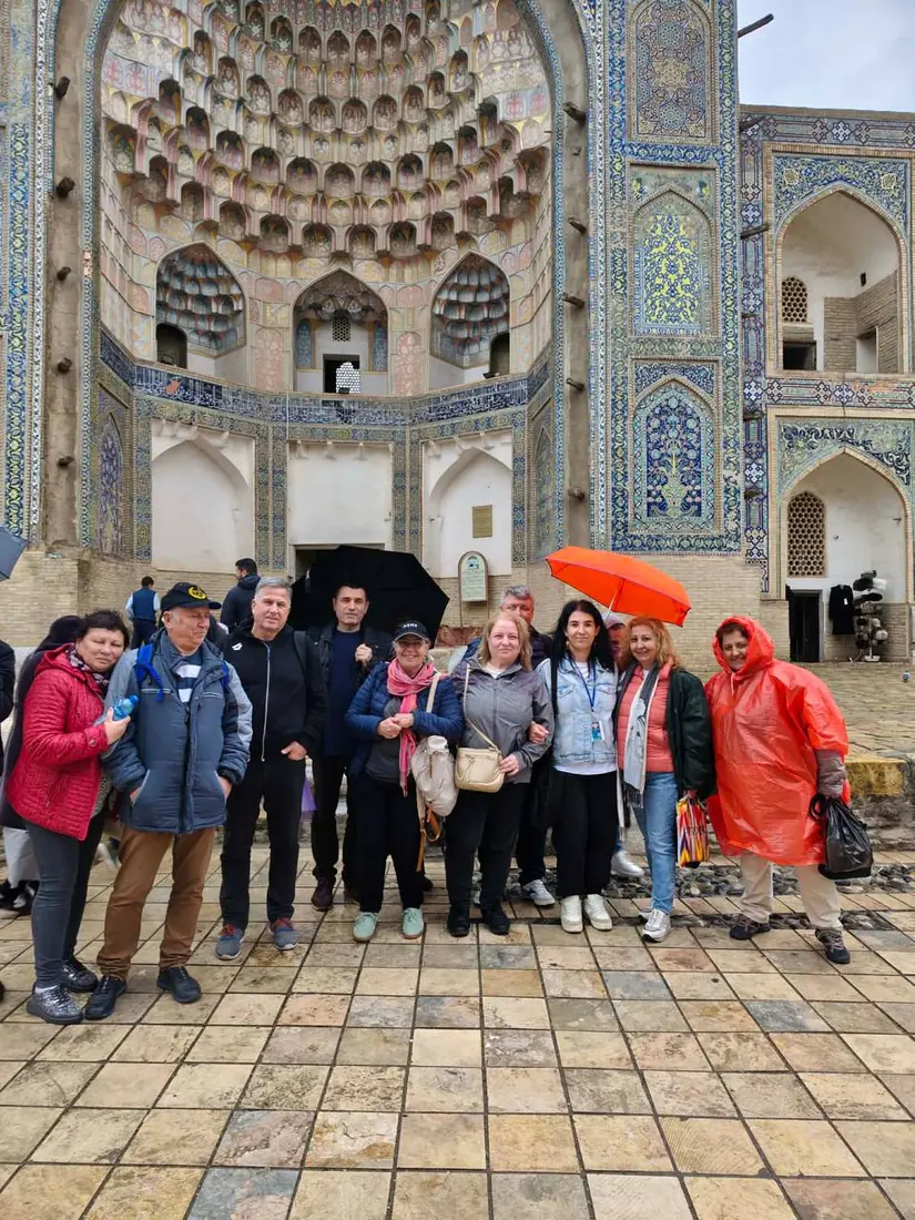 Group tour photo at a Registan portal with colorful umbrellas, Samarkand