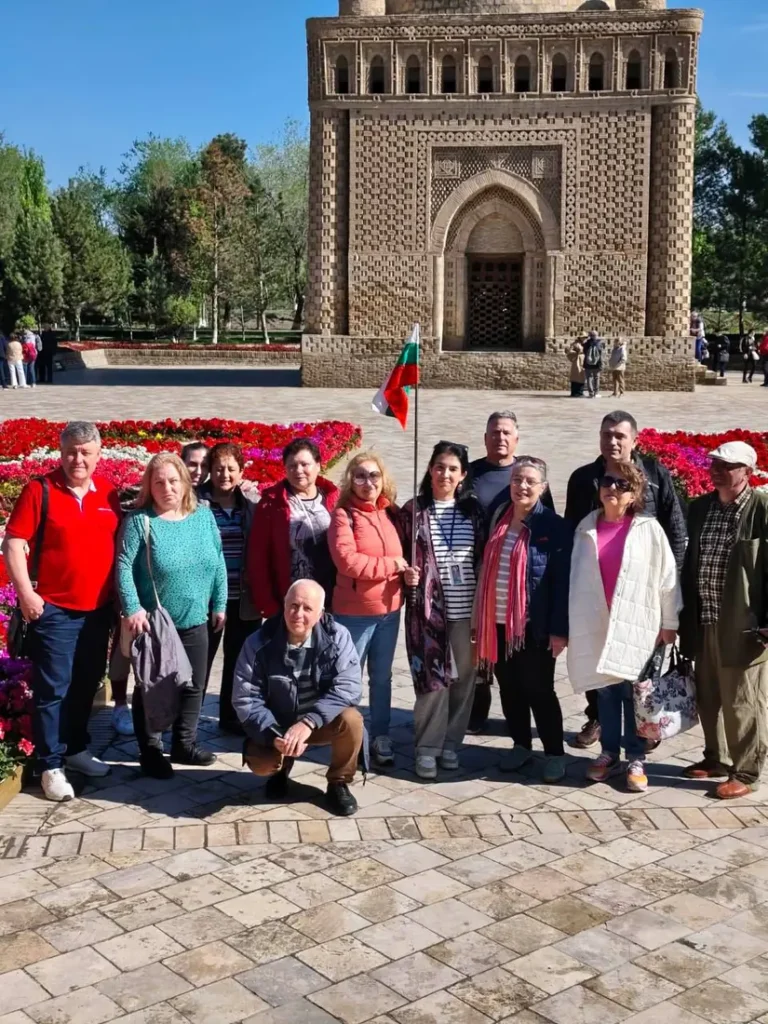 Group tour photo at the Ismail Samani mausoleum with flower beds, Bukhara